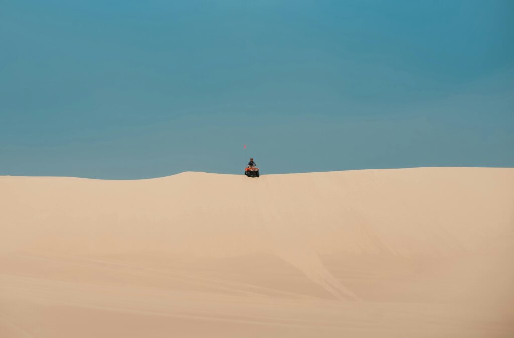 pexels-photo-13641647-13641647 A lone person on an ATV atop a vast sand dune under a clear blue sky, exemplifying adventure and solitude.