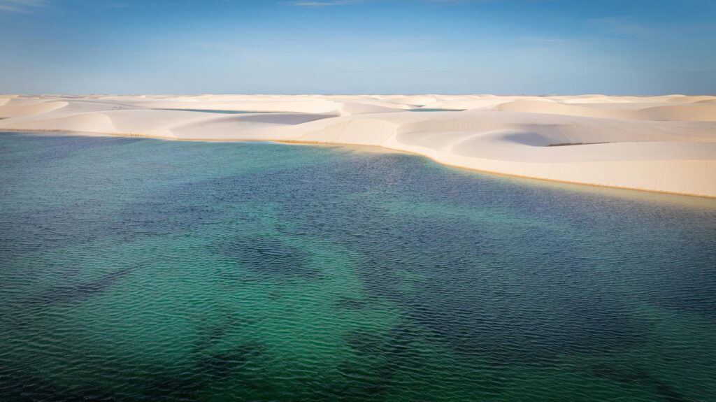 Aerial photo of Barreirinhas sand dunes meeting turquoise waters under a blue sky.