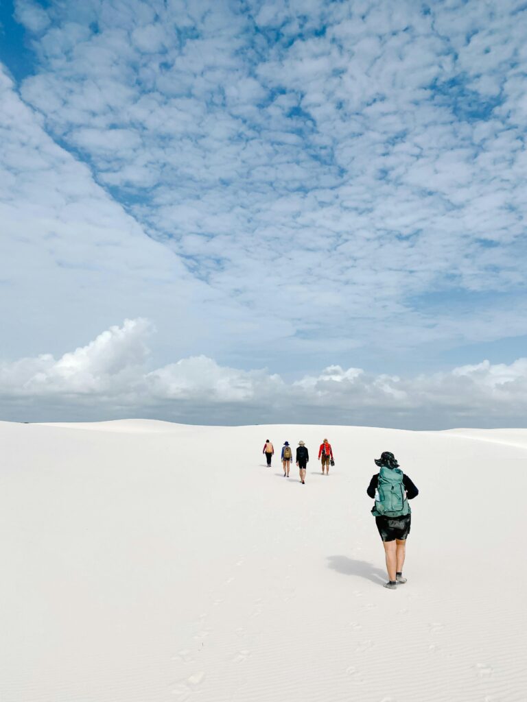 pexels-photo-27990180-27990180 A group of people trekking across vast white sand dunes under a bright blue sky.