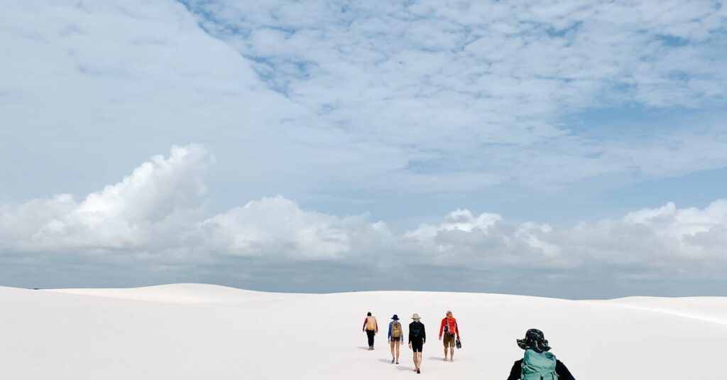 A group of people trekking across vast white sand dunes under a bright blue sky.
