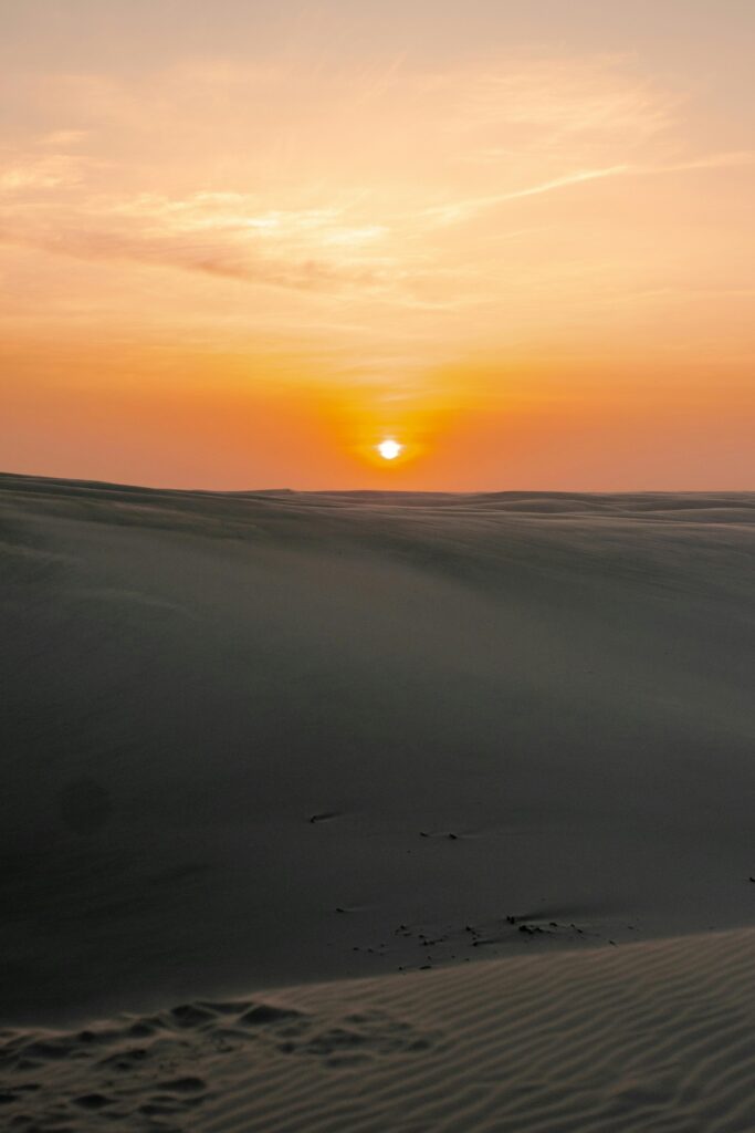A serene sunset casts warm hues over desert dunes in Barreirinhas, Brazil.